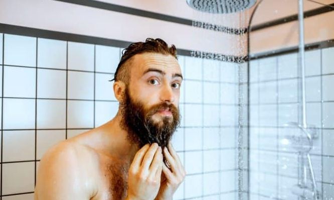 man die de baard schoonmaakt onder de douche