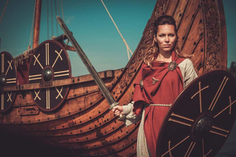 Viking vrouw met haar haar gevlochten draagt een rood gewaad en beige oorlogskleding.