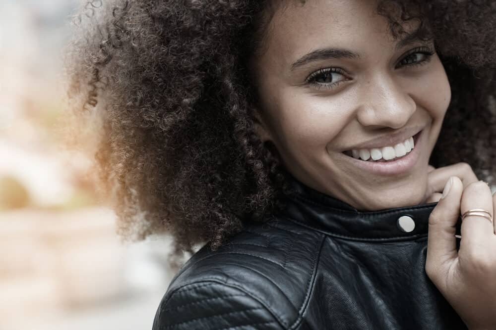 Mooie gemengde vrouw met springerige krullen die een gouden ring aan haar linkerhand draagt