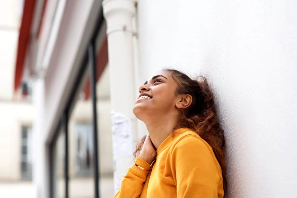 Indiaanse vrouw met een oranje trui en een gouden armband leunend tegen een betonnen muur