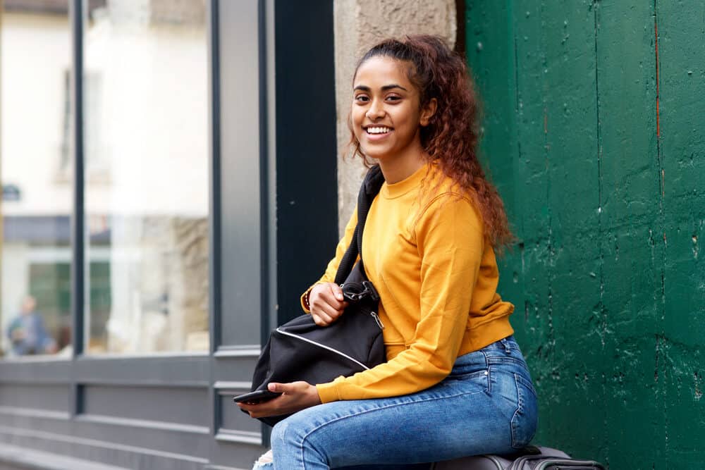 Indiaas meisje klaar om te reizen met een plunjezak, sweatshirt, en gescheurde blauwe jeans