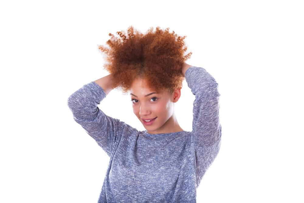 Jonge zwarte dame met een rode haarkleur die een blauwe en witte trui draagt