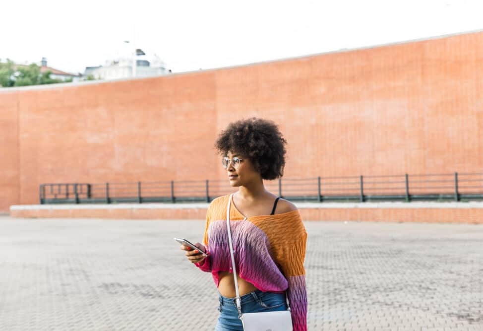 Afro-Amerikaans meisje bekijkt haar mobiele telefoon terwijl ze donkere kleurenkleren draagt.