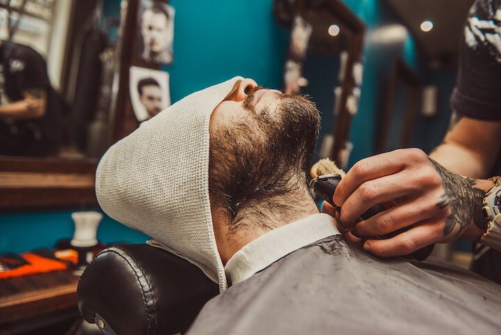 Man met een handdoek op zijn hoofd die zijn baard laat trimmen door een barbier