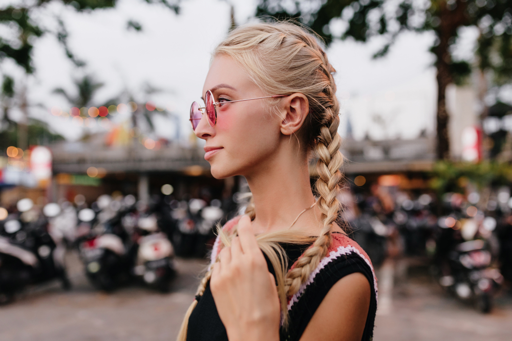 Vrouw met vlechten op een festival in een zwarte tanktop met zonnebril