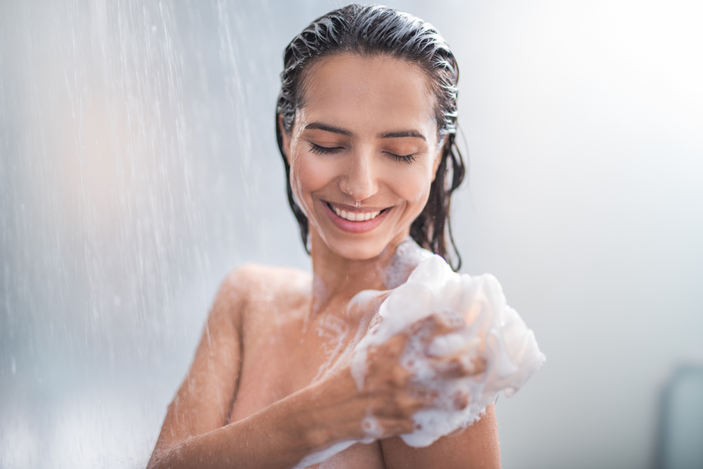 Vrouw die een schuimspons op haar schouder gebruikt voor een stukje over kun je shampoo gebruiken als body wash