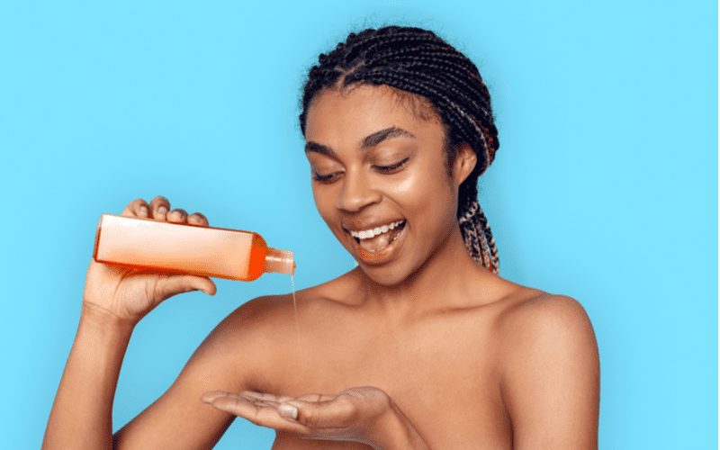 Meisje met vlechten in een blauwe kamer giet de beste shampoo voor vet haar in haar hand