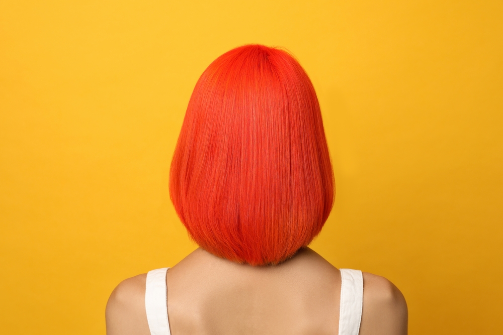 Bold Safety Orange, een van de beste onnatuurlijke haarkleuren voor blauwe ogen, afgebeeld in een witte tank top in een oranje kamer