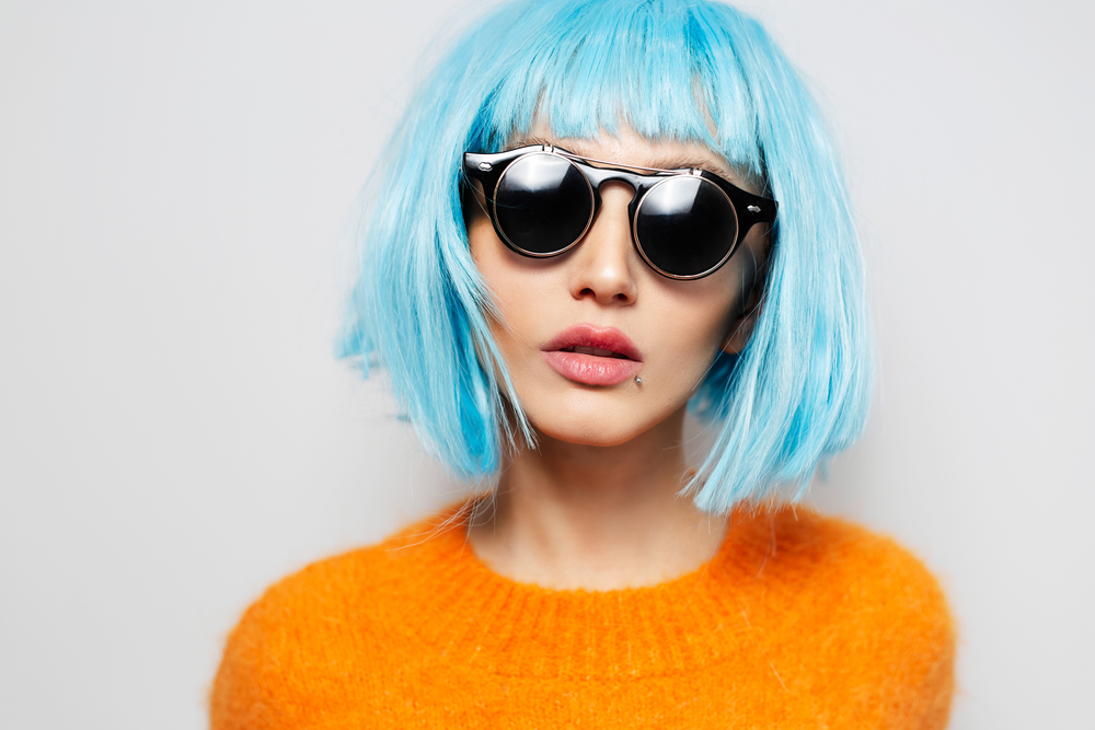 IJsblauw, een top keuze voor onnatuurlijke haarkleuren voor blauwe ogen, op een vrouw in een oranje trui in een grijze kamer
