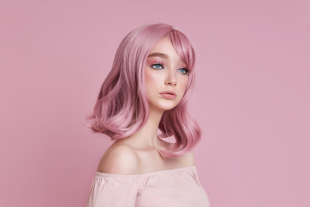 Dusty blush pink, een haarkleur voor blauwe ogen, op een vrouw in een roze kamer die een over-the-shoulder shirt draagt