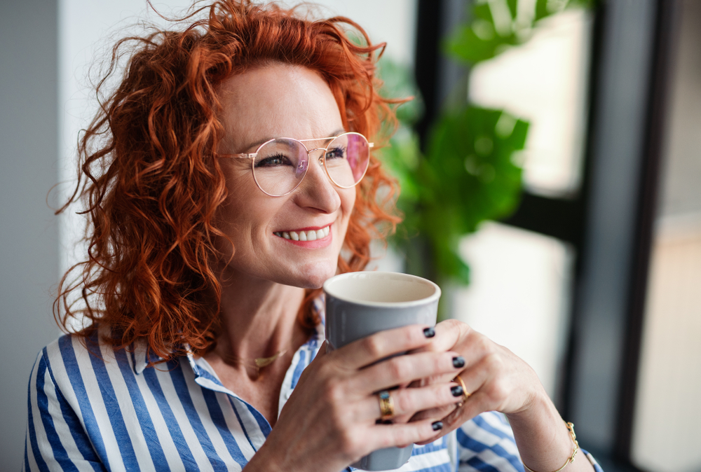 Als een van de beste haarkleuren voor grijs haar, drinkt een vrouw met Bold, Vibrant Copper All-Over Color een koffie