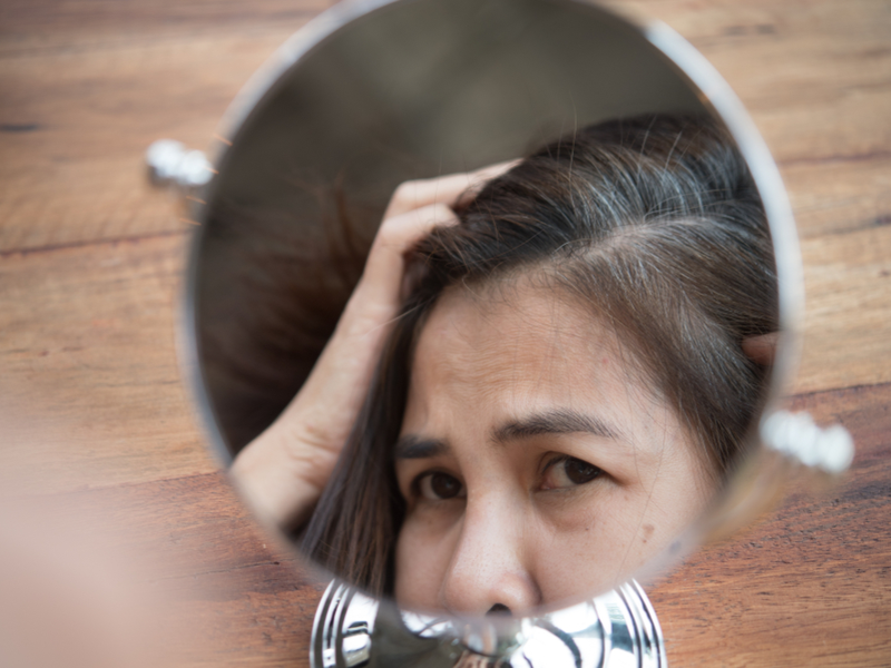 Vrouw die walnootolie tegen grijs haar heeft gebruikt kijkt in de spiegel