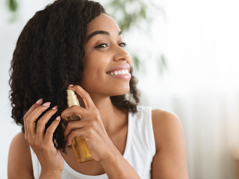 Gelukkige zwarte vrouw gebruikt macadamia olie vs argan olie voor haar