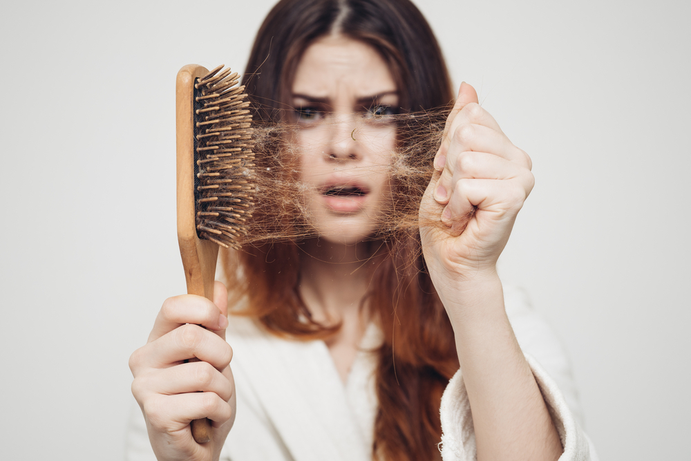 Vrouw die een borstel tegen de camera houdt voor een stuk getiteld How Many Hair Strands Are on a Head