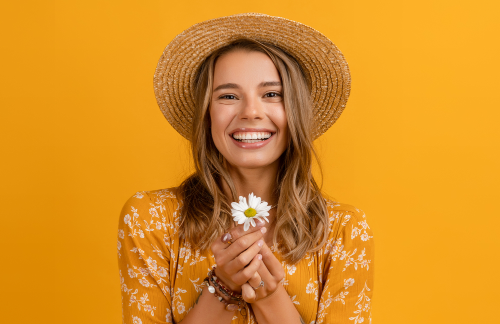 Golden Bronde zomer haarkleur op een vrouw met een hoed in een oranje kamer