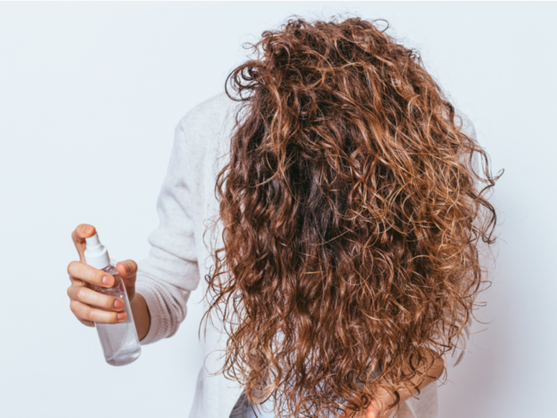 Vrouw die een ontklittende spray gebruikt op haar matte haar voor een stuk over hoe mat haar te ontklitten