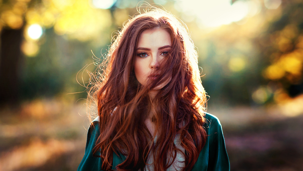 Vrouw met rood haar, een van de beste haarkleuren voor blauwe ogen, sensueel staand in een bos