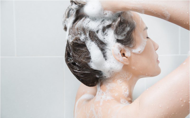 Aziatische vrouw die haar haar shampoot in voorbereiding om het te plagen zodra zijn droog en schoon