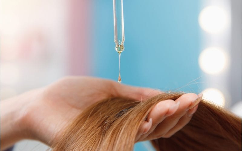 Vrouw die haarserum op haar haar aanbrengt terwijl ze het in haar handen houdt