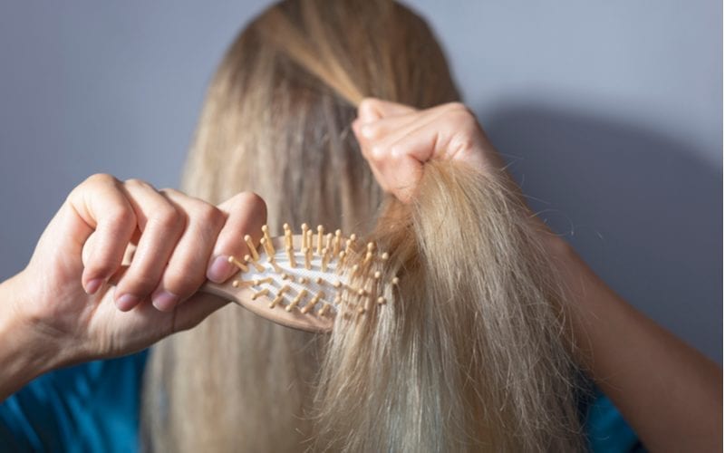 Beeld van een blonde vrouw die haar fijn haar kamt na gebruik van kokosolie