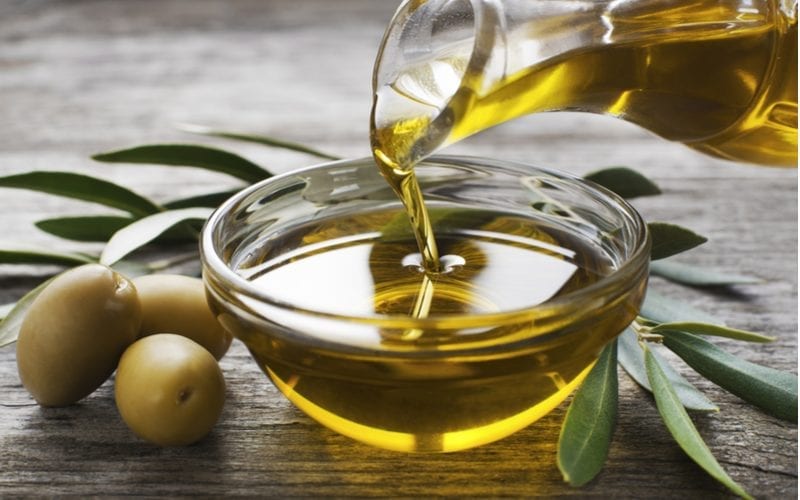 Olijven en olijfolie liggen op een houten tafel naast groene bladeren