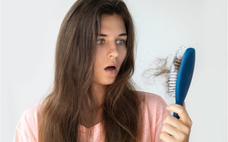 Jonge dame kijkt naar haar haarborstel voor een stukje over waarom ze een appelciderazijn haarspoeling had moeten gebruiken