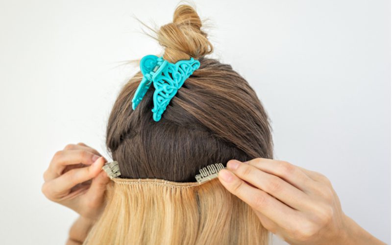 Dame met clip-in hair extensions heeft haar haar omhoog in een knot en de knot geklemd door een teal clip