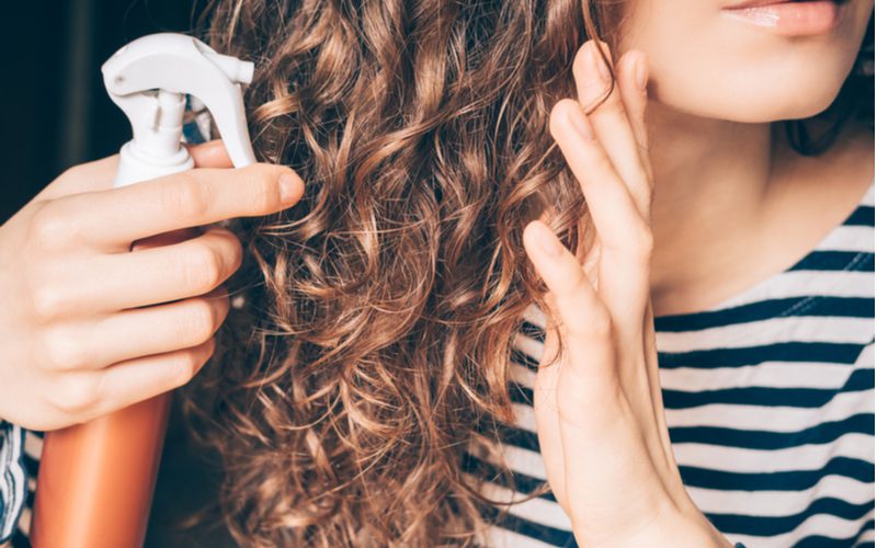 Dame spuit styling crème in haar krullend haar met een marine en wit shirt om de tweede stap in het diffuseren van haar te symboliseren.