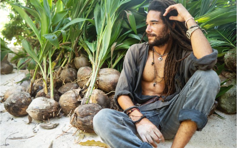 Man die net geleerd heeft hoe je dreads moet vormen zit op een strand met zijn hand in zijn haar