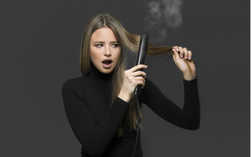 Vrouw wiens haar verbrand ruikt kijkt naar de rook van een strijkijzer