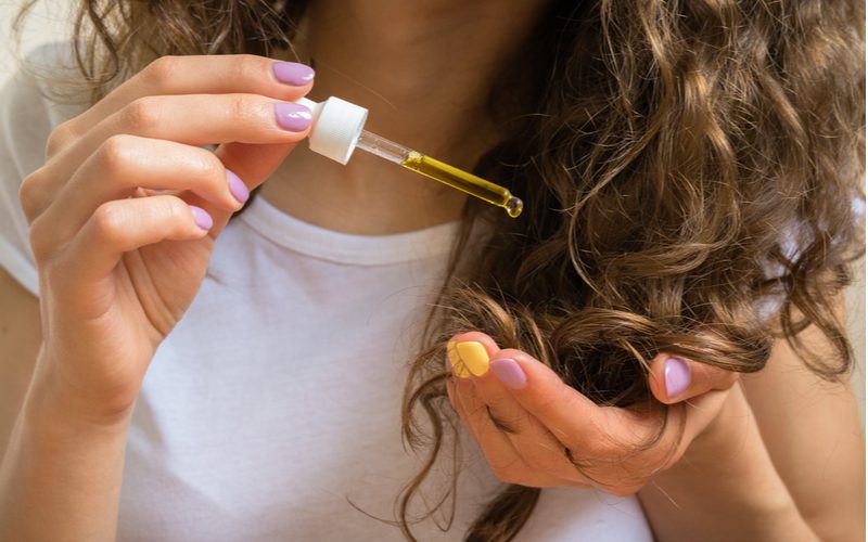 stap 3 in de gids hoe beschadigd haar te herstellen toont een vrouw die haarolie op haar haar druppelt.