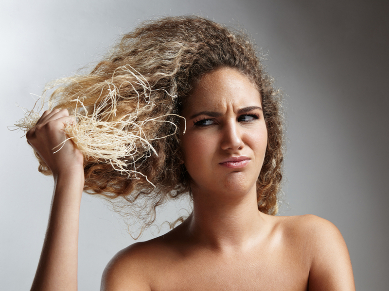 Vrouw met beschadigd haar dat gomachtig is na het bleken houdt haar stroeinden vast