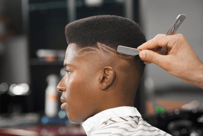 Afro-Amerikaanse man met een high top fade zit in de kappersstoel en wordt geschoren met een scheermes.