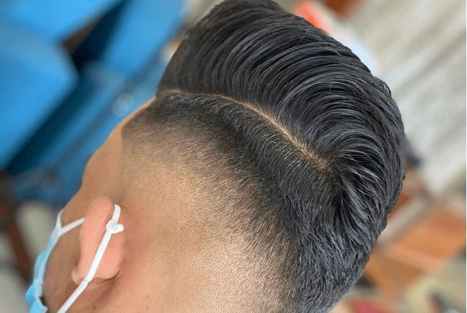 Man met een mohawk pointed drop fade zit in een kappersstoel met een masker op en kijkt recht vooruit.