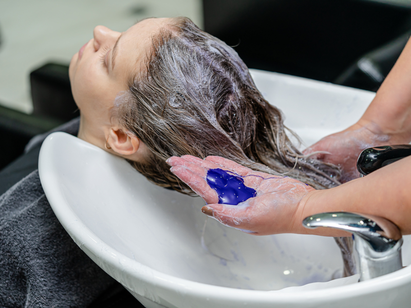 Vrouw repareert een slechte peroxide haarverf met paarse shampoo in de salon