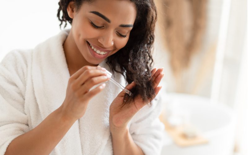 Als afbeelding voor een post over hoe te vertellen of je haarschade hebt, een vrouw die haarserum op het uiteinde van haar haar doet