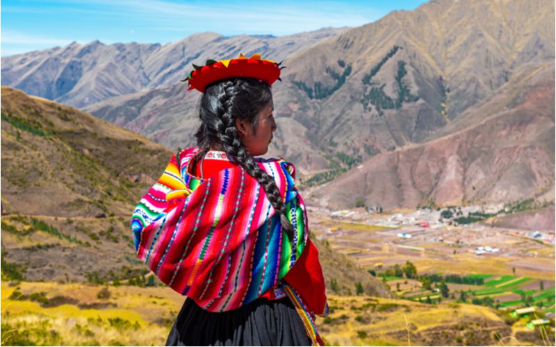 Peruaanse vrouw staat in een bergketen en kijkt uit over een stad beneden