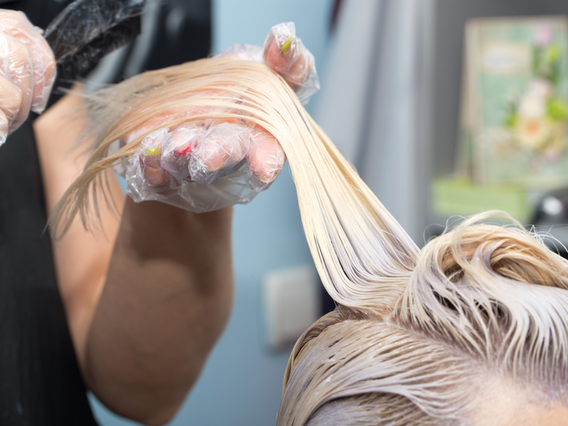 Kapper blondeert het haar van een vrouw met bleekmiddel