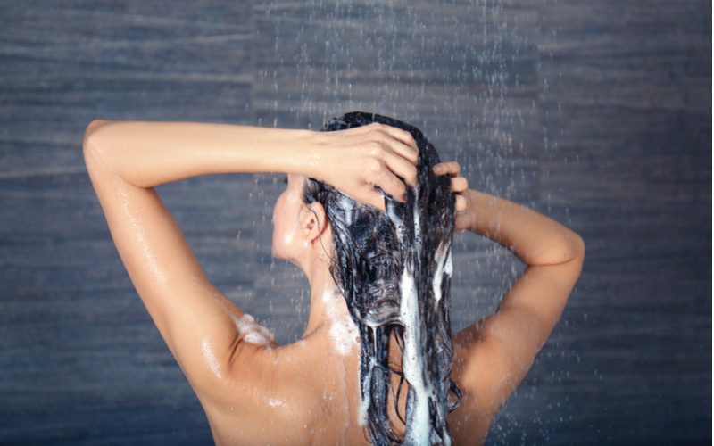 Afbeelding voor een stuk over hoe je van vet haar afkomt met een vrouw onder de douche die haar haar wast.