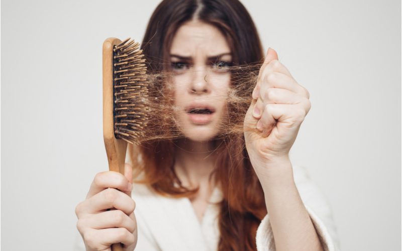 Meisje dat een bos lang bruin haar van een houten haarborstel trekt voor een stukje over het wegwerken van vet haar