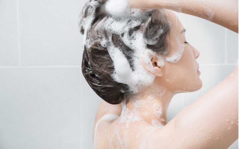 Aziatische vrouw sluit haar ogen tijdens het wassen van haar haar in een grijze betegelde douche