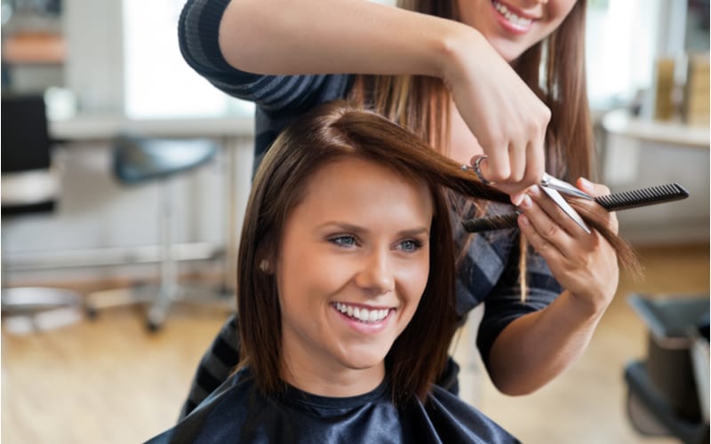 Gelukkige jonge vrouw die een nieuw kapsel krijgt van kapper bij salon om te helpen illustreren hoe een kapsel te krijgen