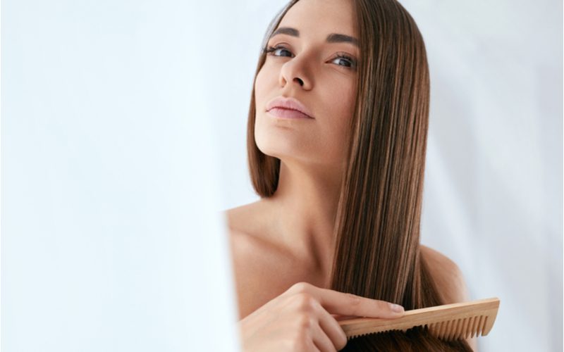 Euro vrouw met een houten kam trekt deze door haar haar terwijl ze omhoog en naar links kijkt