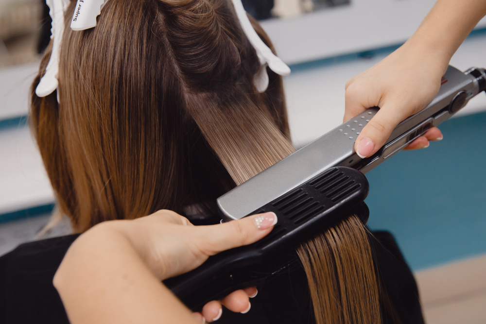 Vrouw krijgt een keratine behandeling met heet gereedschap in een salonstoel