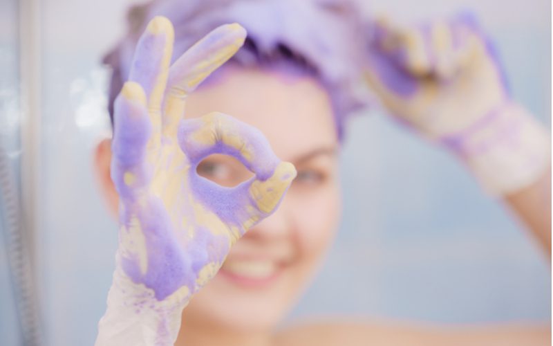 Vrouw verwijdert paarse shampoovlek uit haar haar en geeft een ok teken met haar vingers