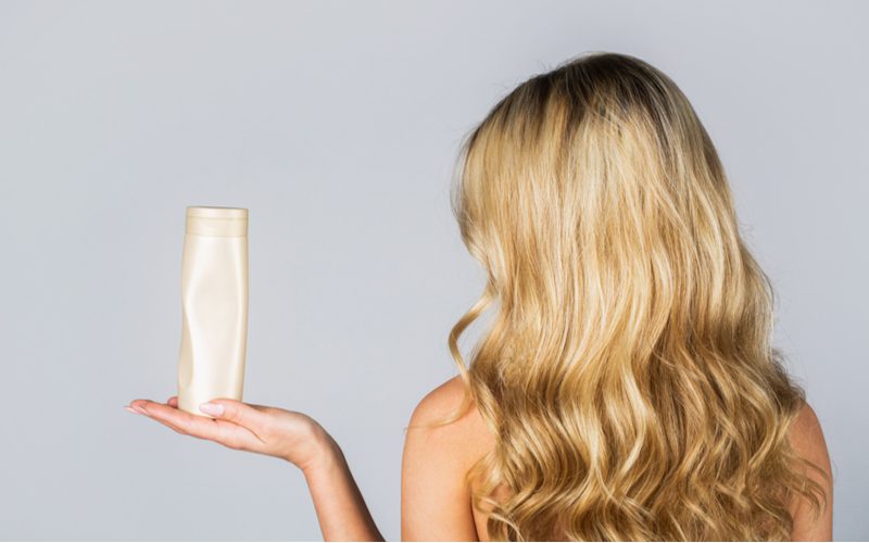 Vrouw houdt een fles verhelderende shampoo vast om overkleurd haar te herstellen