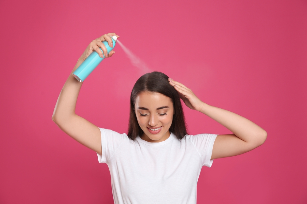 Vrouw die droogshampoo gebruikt als alternatief voor haarlak in een roze kamer