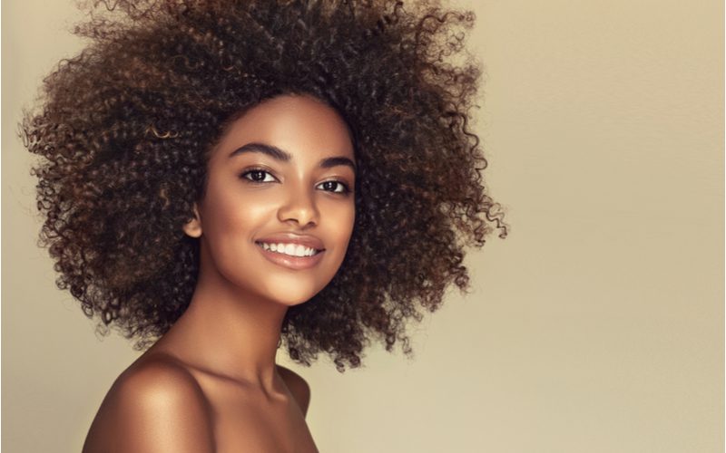 Voor een stuk over pruiken voor zwarte vrouwen, zit een meisje met kinky haar in een afro in een bruine studio