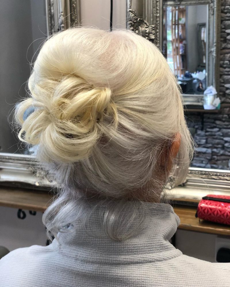 Fancy Updo op het haar van een blonde vrouw in een witte coltrui vermeld als een idee voor een bruiloftsgast kapsel