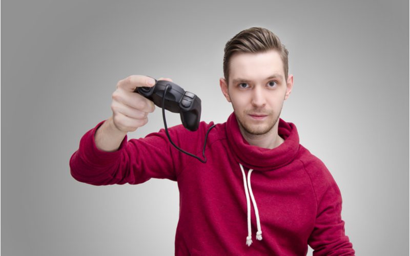 Man met gladgestreken haar in een rode hoodie die een gaming controller omhoog houdt